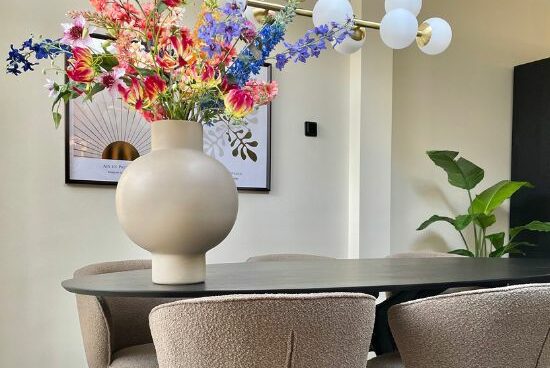 Zwart ovale eettafel beige bouclé eetkamerstoelen beige ronde vaas met fleurig boeket kunstbloemen